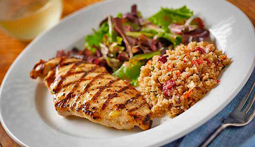 Arroz integral, frango grelhado, salada em um prato branco de porcelana.